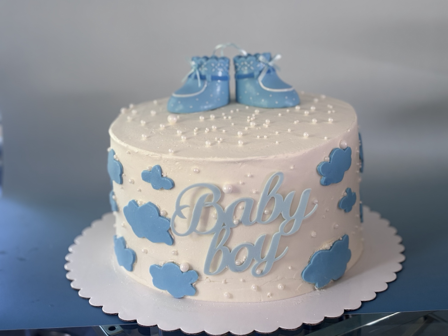 Yilda’s white baby shower cake with blue clouds, tiny blue baby shoes and pearl details